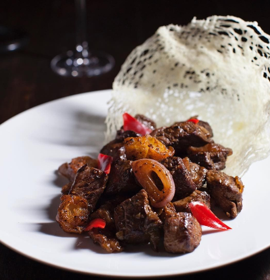 A plate featuring crispy, seasoned beef bites with red chili slices, served with a mound of shredded white rice atop a white plate.