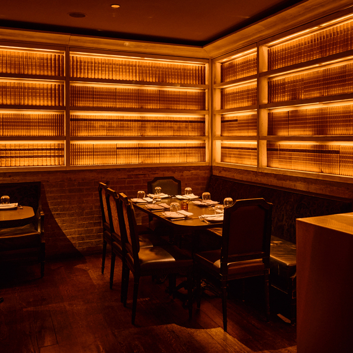 Cozy restaurant booth with reddish lighting, wood paneling, and a table set for two.